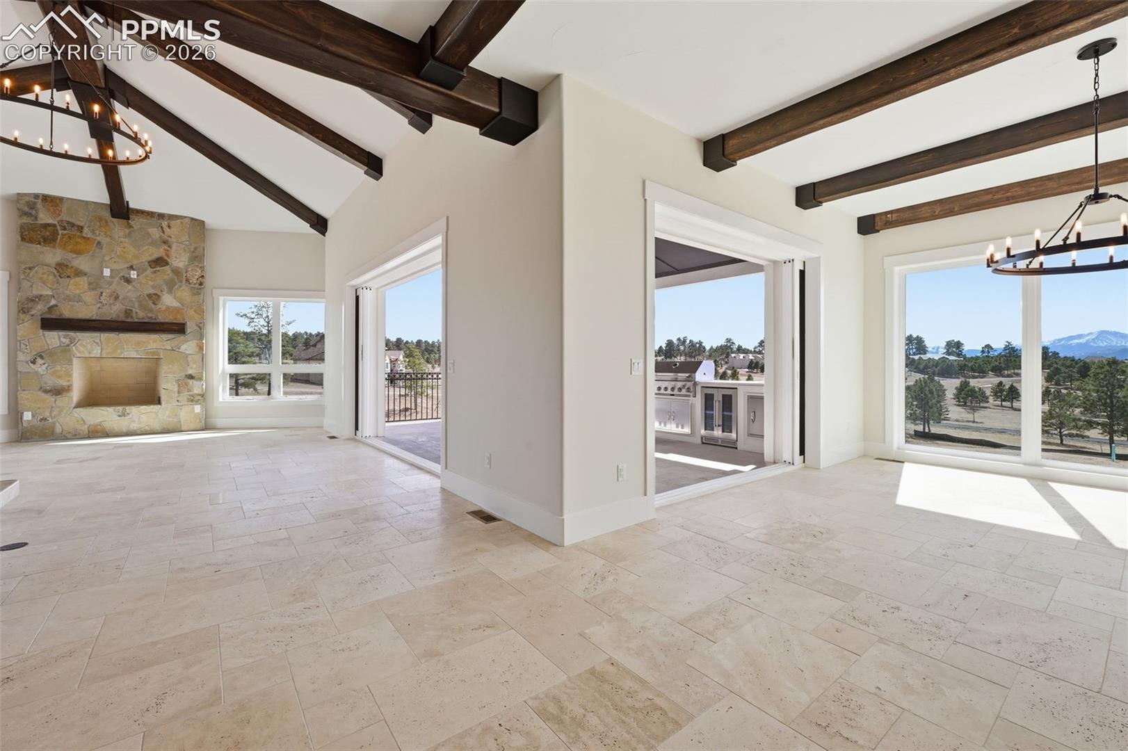 Unfurnished living room with suspended lighting, stone tile flooring, beam ceiling, and a fireplace. Dining Room on right side. Note: retractable window walls.