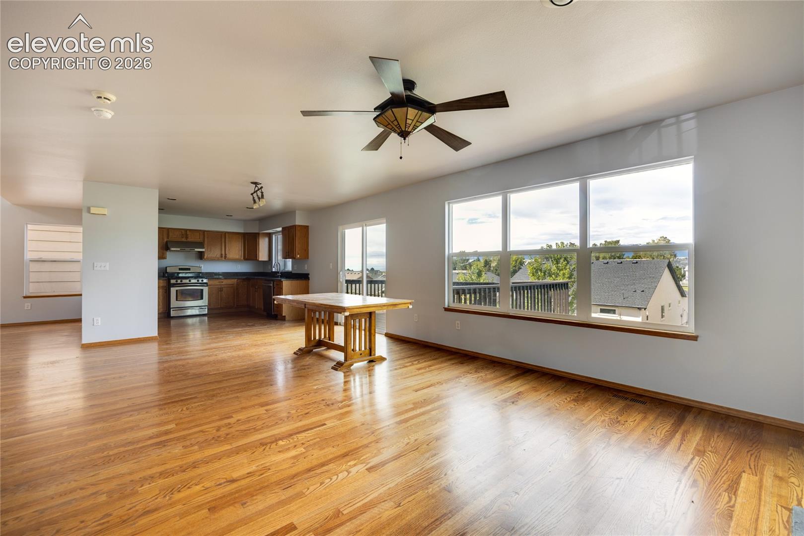 Open-concept living area featuring wood-finish flooring, a ceiling fan with light, and extensive windows