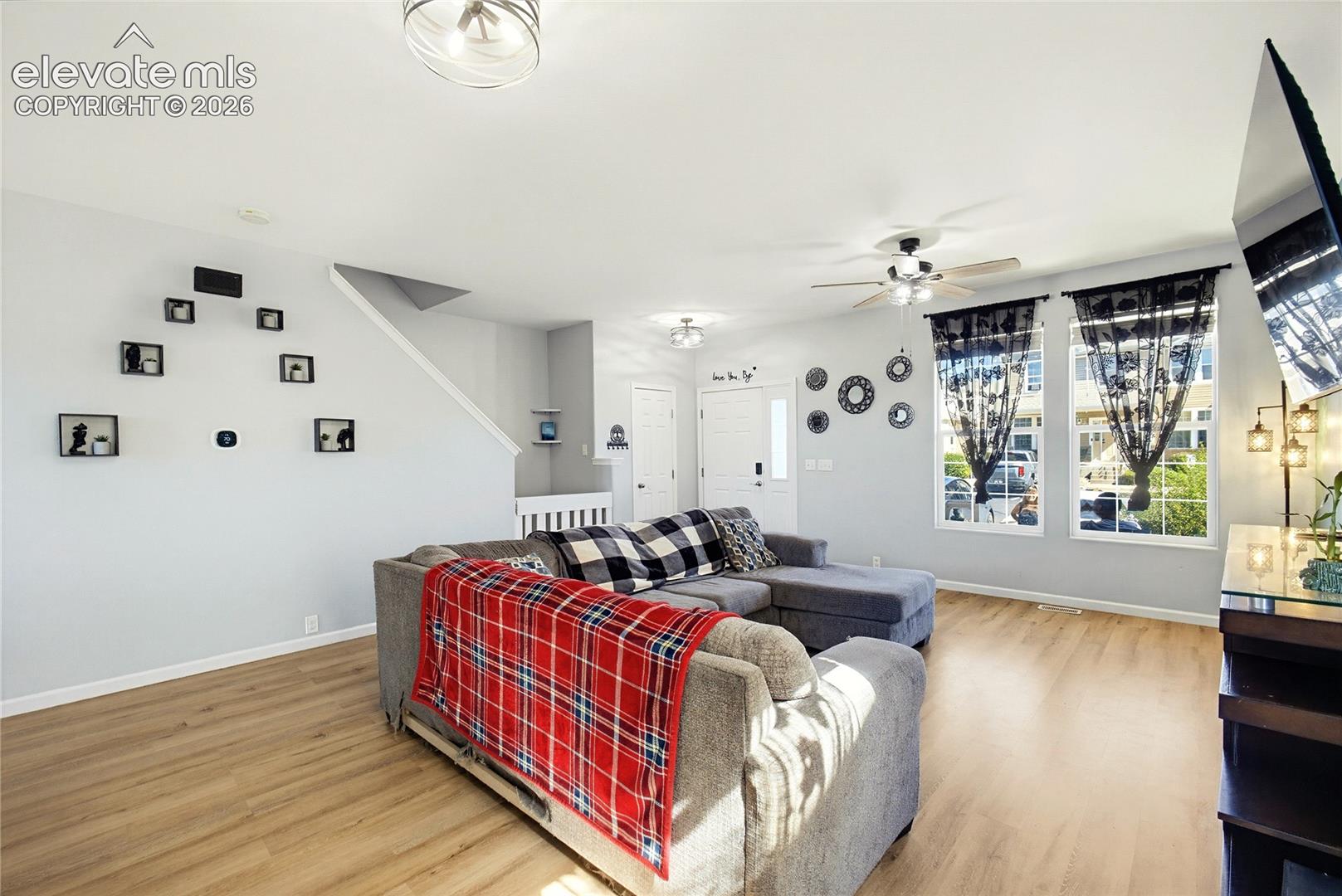 Open-concept living area featuring wood-finish flooring, a ceiling fan with integrated lighting, and multiple windows