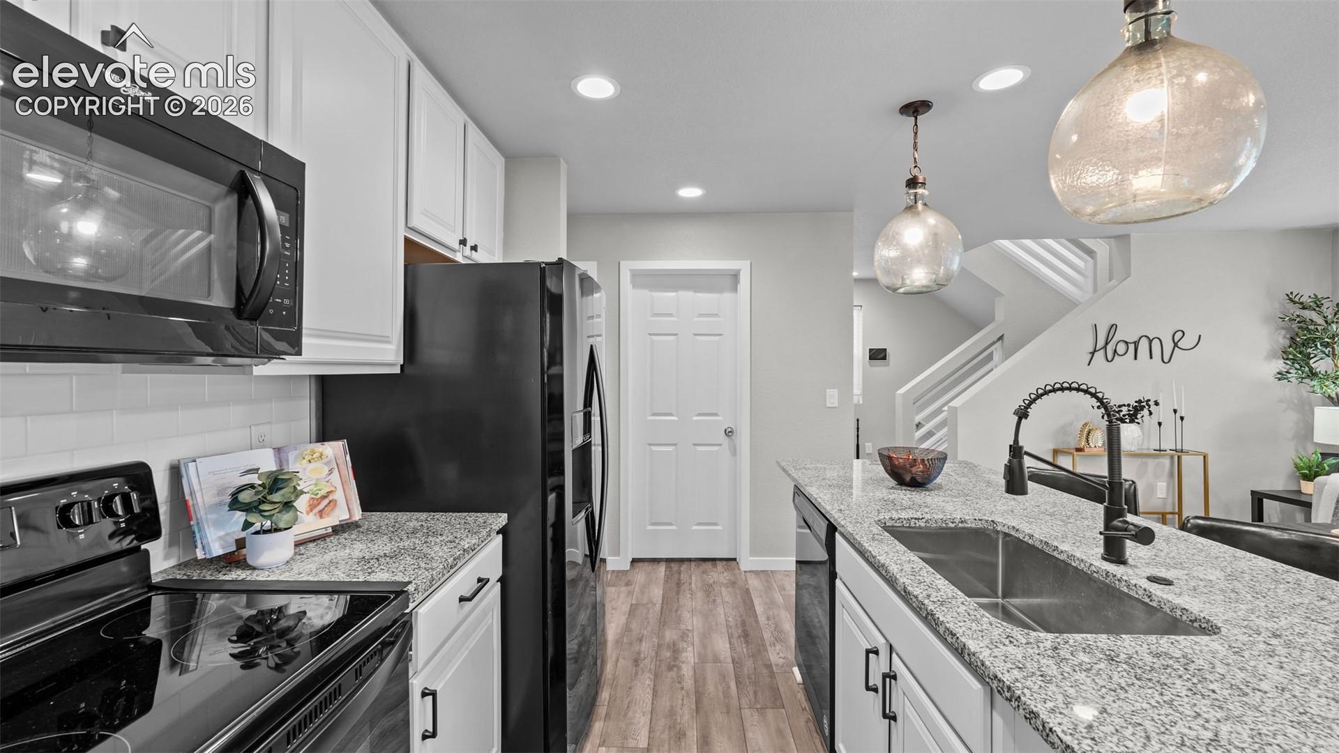 Kitchen featuring white shaker-style cabinetry, stone-finish countertops, subway tile backsplash, wood-finish flooring, and pendant lighting
