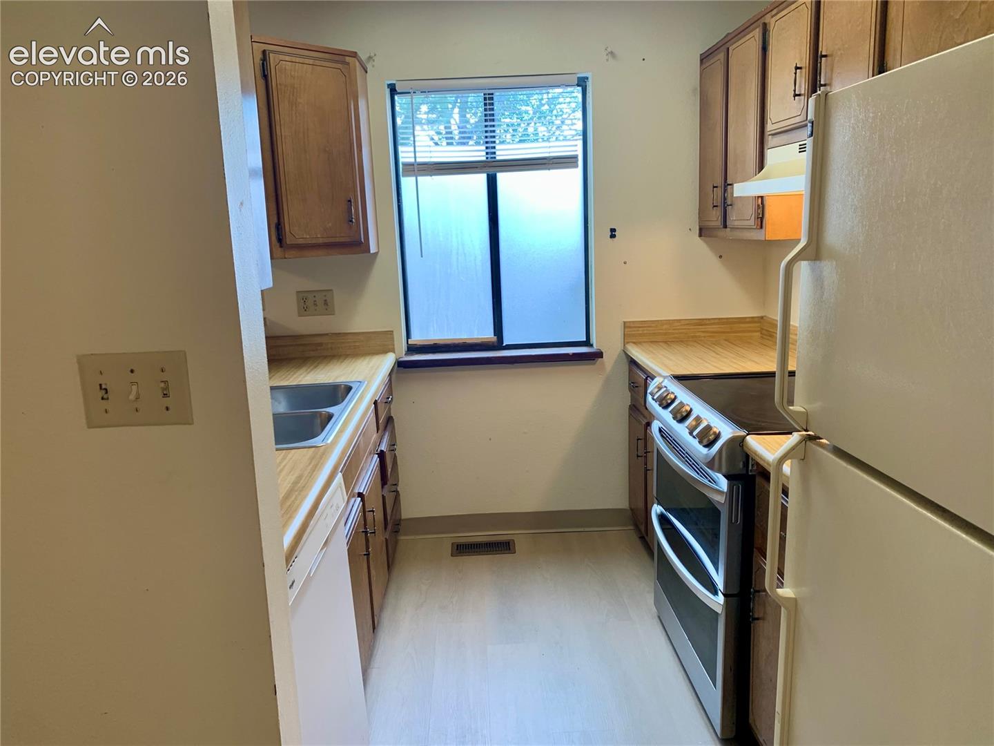 Galley kitchen featuring wood-finish cabinetry, a double basin sink, and a four-burner range with an oven