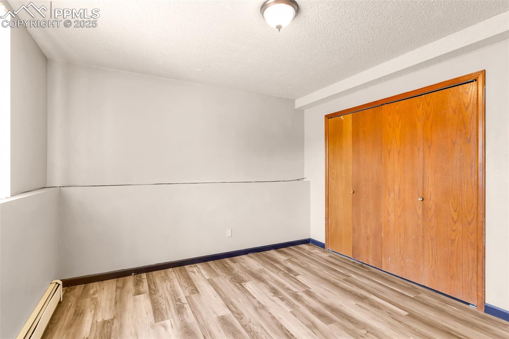 Unfurnished bedroom with a baseboard radiator, light wood finished floors, a textured ceiling, and a closet
