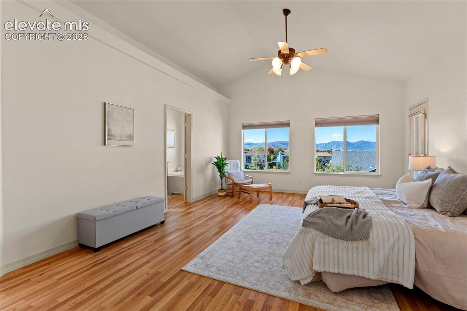 Vaulted ceilings featuring a central overhead fan, wood-finish flooring, and large windows with a mountain backdrop