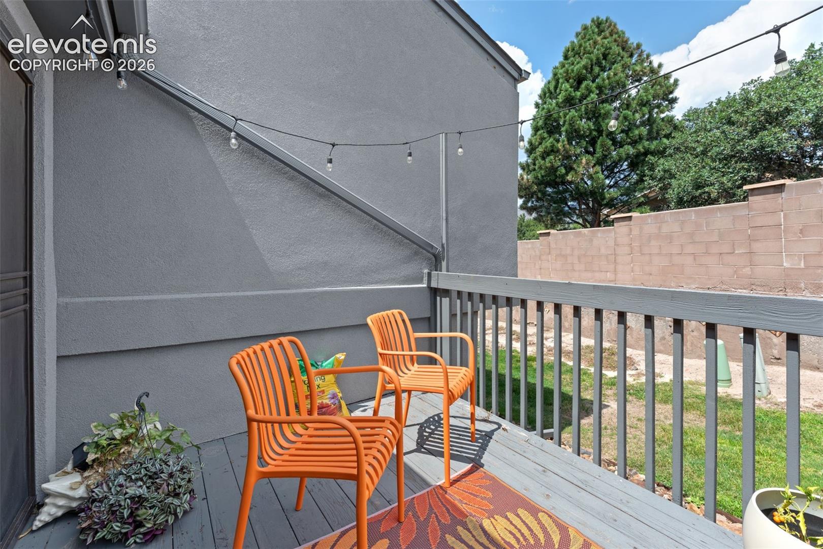 Wood-finish deck with a painted railing, string lighting, and a partial privacy wall