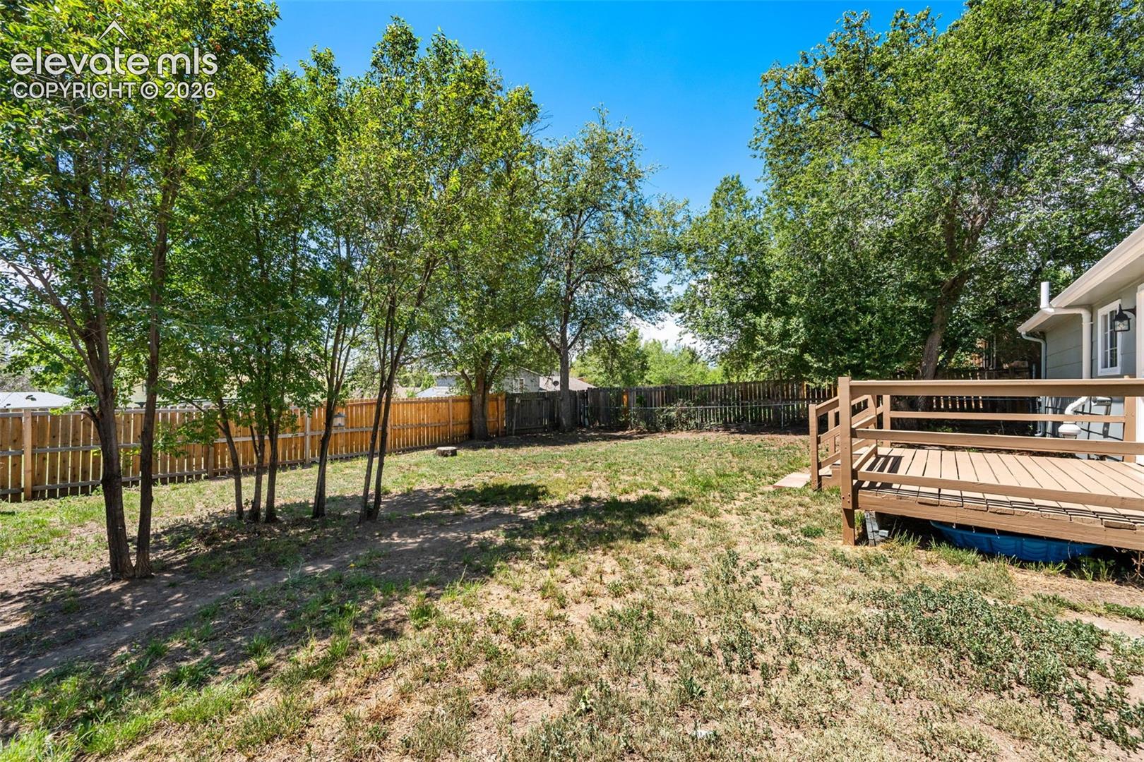 Expansive backyard featuring a wood deck, mature trees, and privacy fencing
