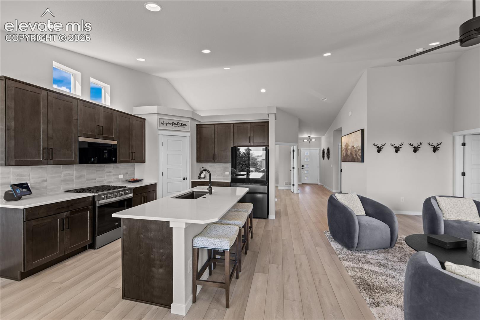 Kitchen featuring dark-toned cabinetry, light-colored countertops, a center island with integrated sink, wood-finish flooring, and vaulted ceilings