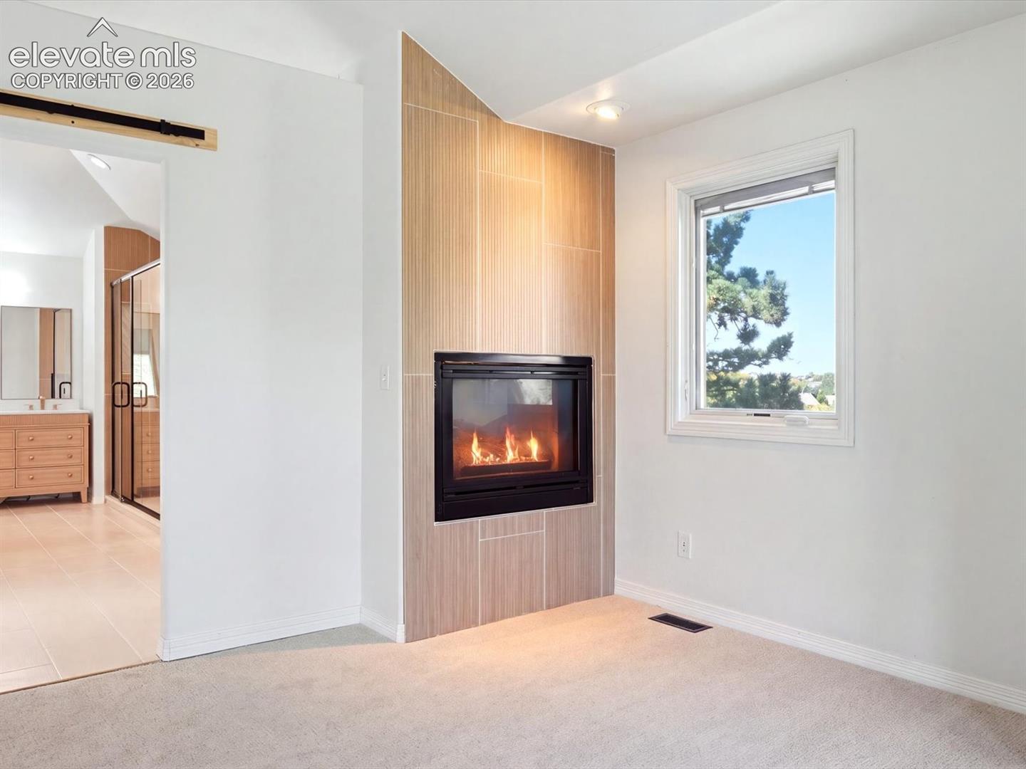 Fireplace featuring floor-to-ceiling neutral tile surround, black metal firebox, recessed ceiling lighting, and sliding barn-door hardware