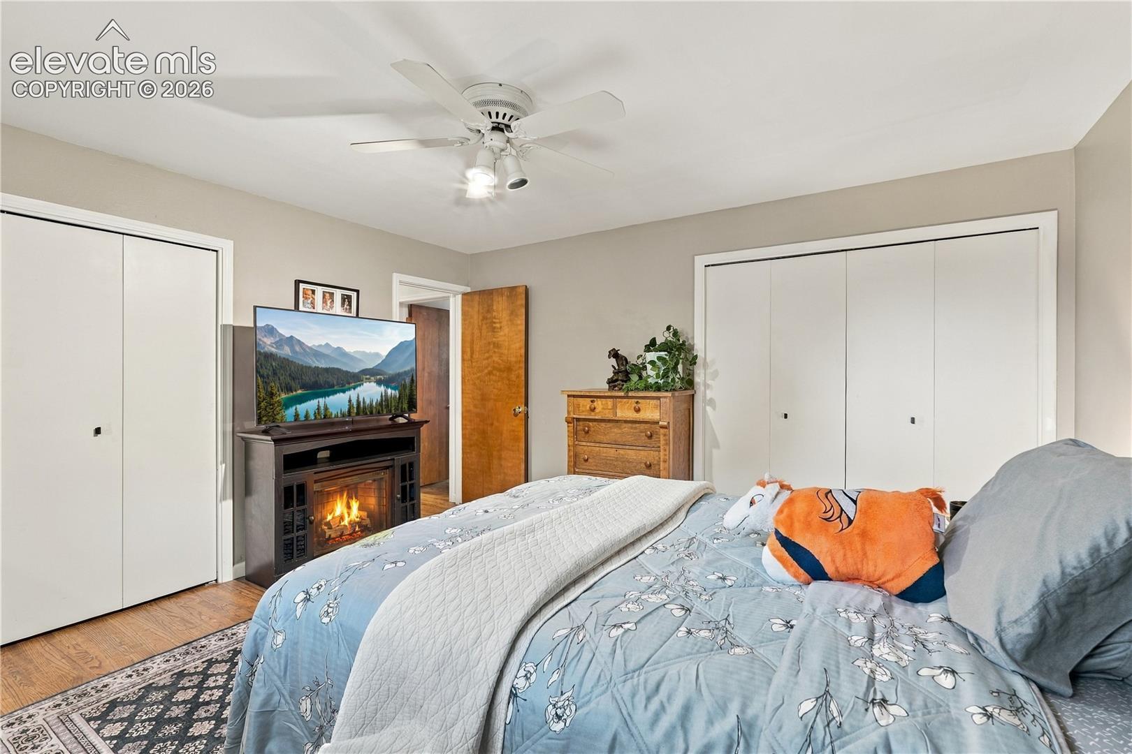 Room featuring dual sets of double-door closets, wood-finish flooring, and a ceiling fan with integrated lighting