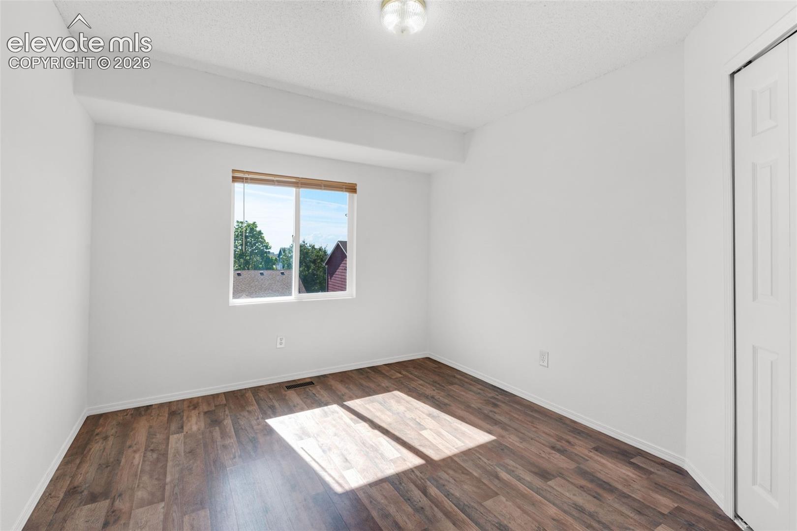 Recessed window with wood-tone blinds, wood-finish flooring, overhead flush-mount lighting, and bi-fold closet doors