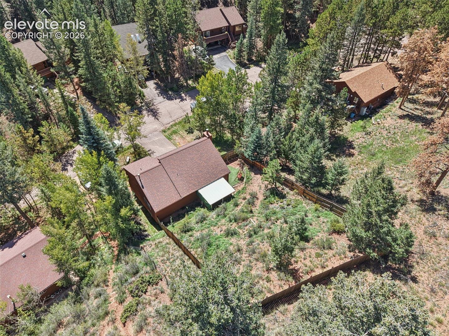 Wood-sided property with a brown shingle roof, accompanied by mature evergreen trees