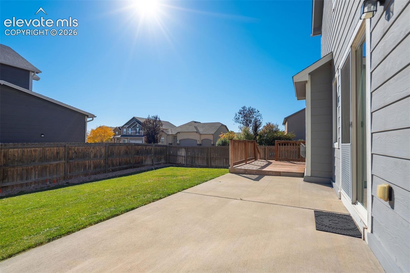 Private backyard with a wooden fence, concrete patio, and an elevated wooden deck