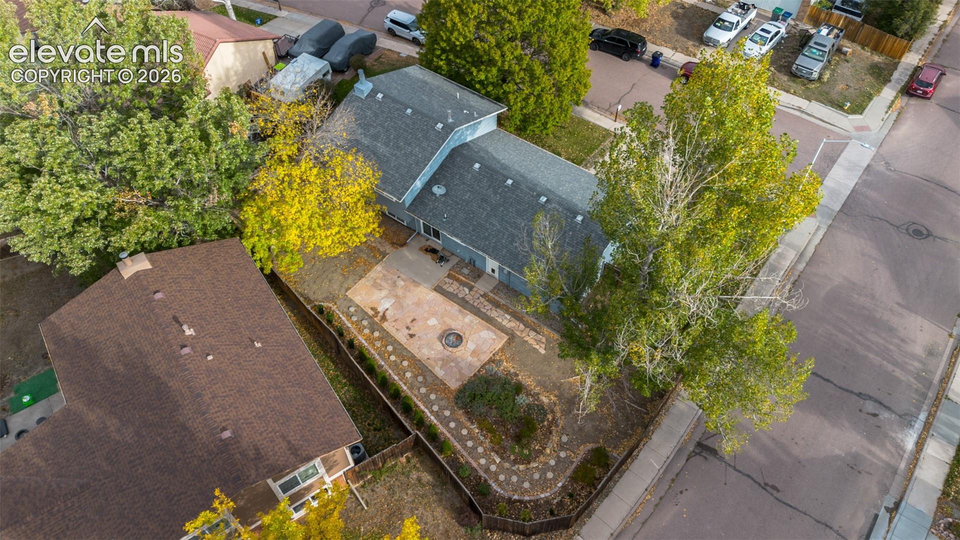 Aerial view of property featuring a rear patio, built-in fire pit, stone-accented walkway, and mature landscaping