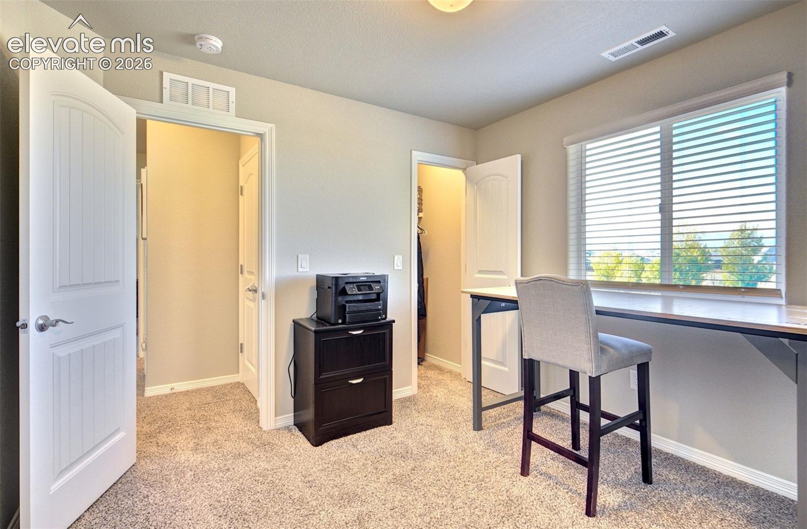 Neutral-toned interior featuring wall-to-wall carpeting, white paneled interior doors, and a built-in window-side workstation