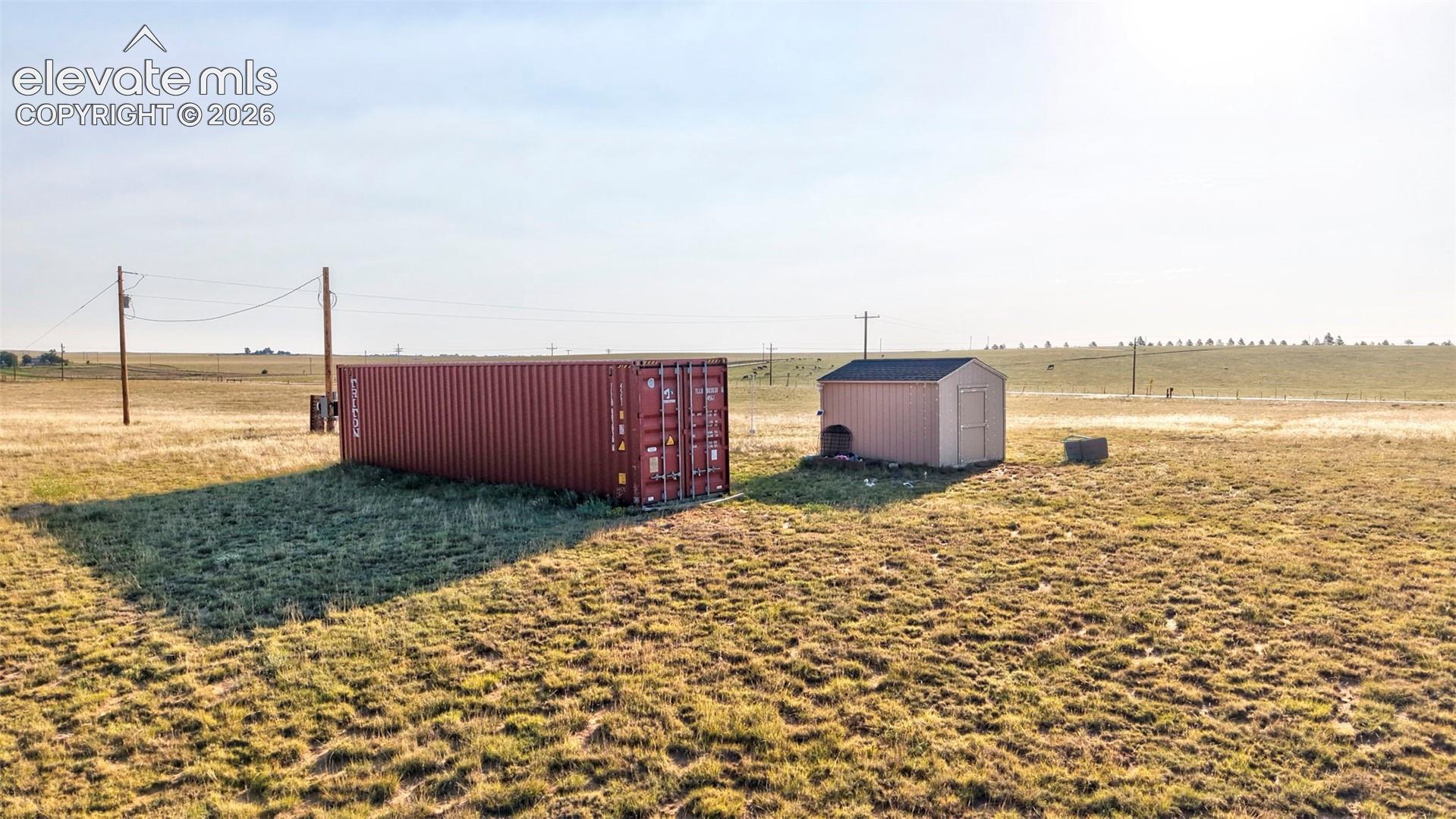 Expansive open land featuring a red shipping container and a tan storage shed