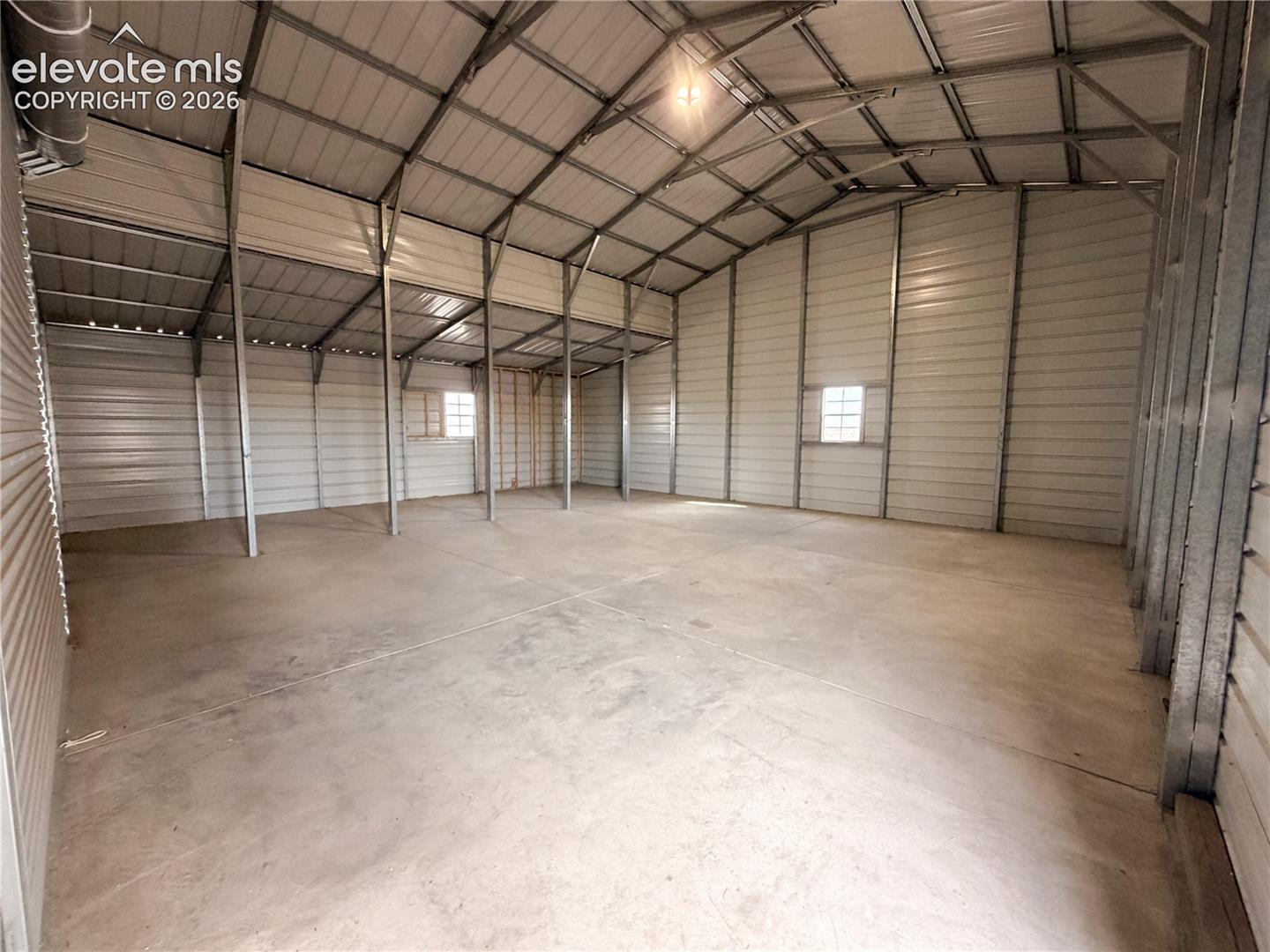Expansive metal-framed structure featuring a concrete slab foundation, high-clearance vaulted ceilings, metal siding, and multiple windows