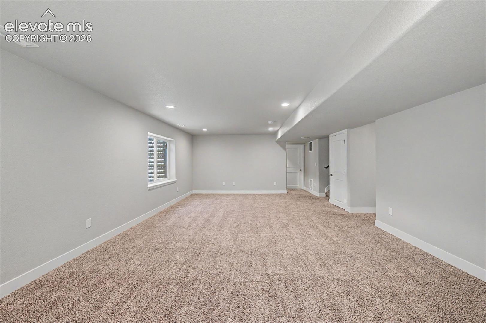 Expansive carpeted area featuring recessed lighting, a single window with horizontal blinds, and white trim throughout