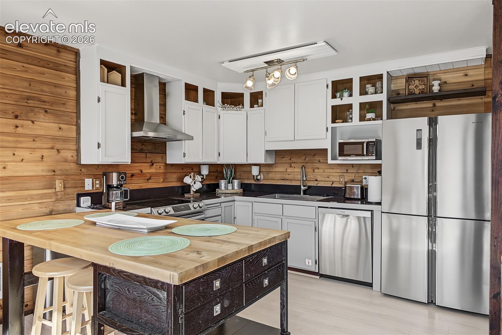 Kitchen featuring wood-paneled walls, white cabinetry, dark countertops, a stainless steel refrigerator, and a stainless steel range hood