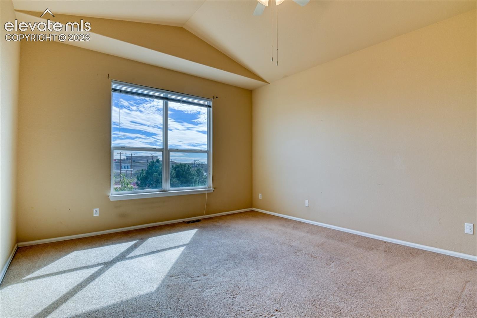 Vaulted ceiling with an integrated white ceiling fan, large picture window, and neutral carpeting