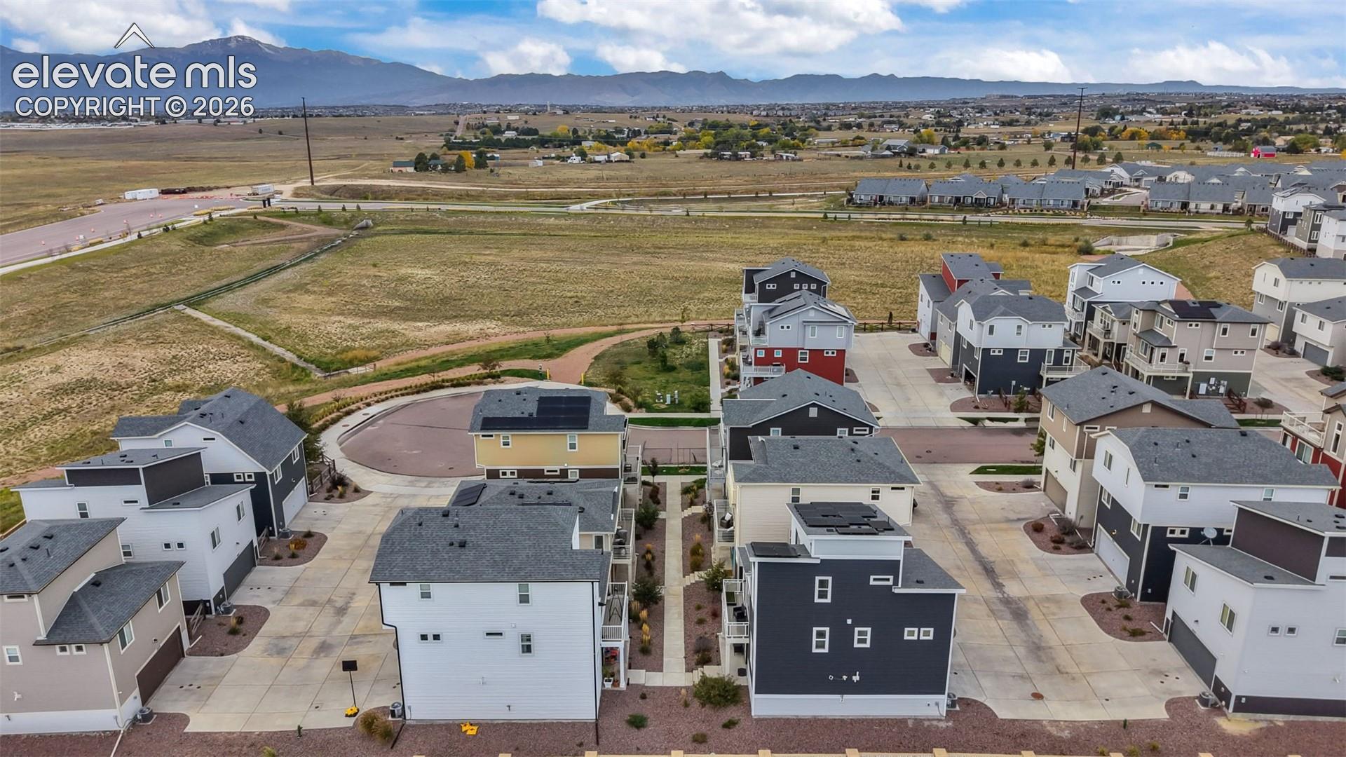 Aerial perspective of a multi-structure property featuring high-contrast architectural siding, integrated rooftop solar arrays, shingled roofing, concrete paved driveways, and expansive mountain scenery
