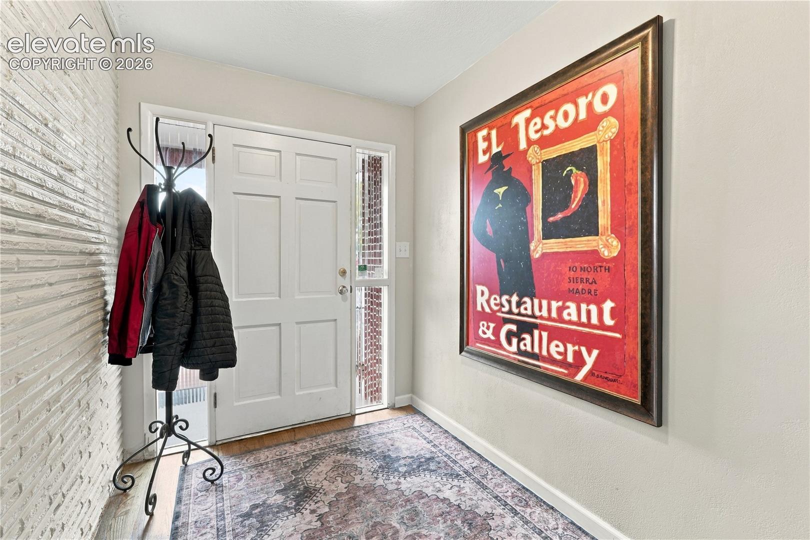 Entryway featuring a solid panel front door, flanking vertical glass sidelight, and white textured brick accent wall
