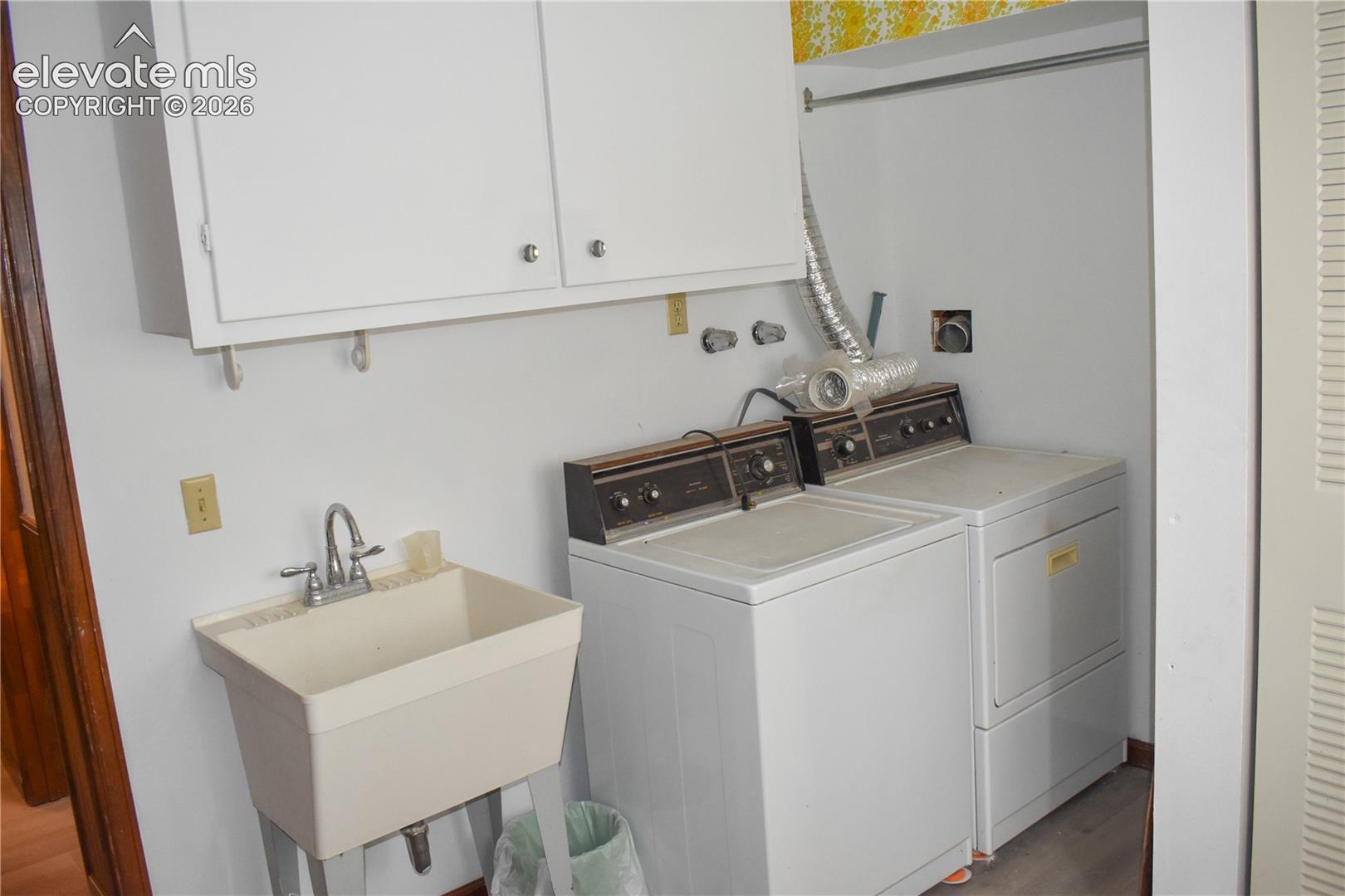 Utility area featuring wall-mounted cabinetry, a utility sink with dual-handle faucet, and bi-fold louvered doors