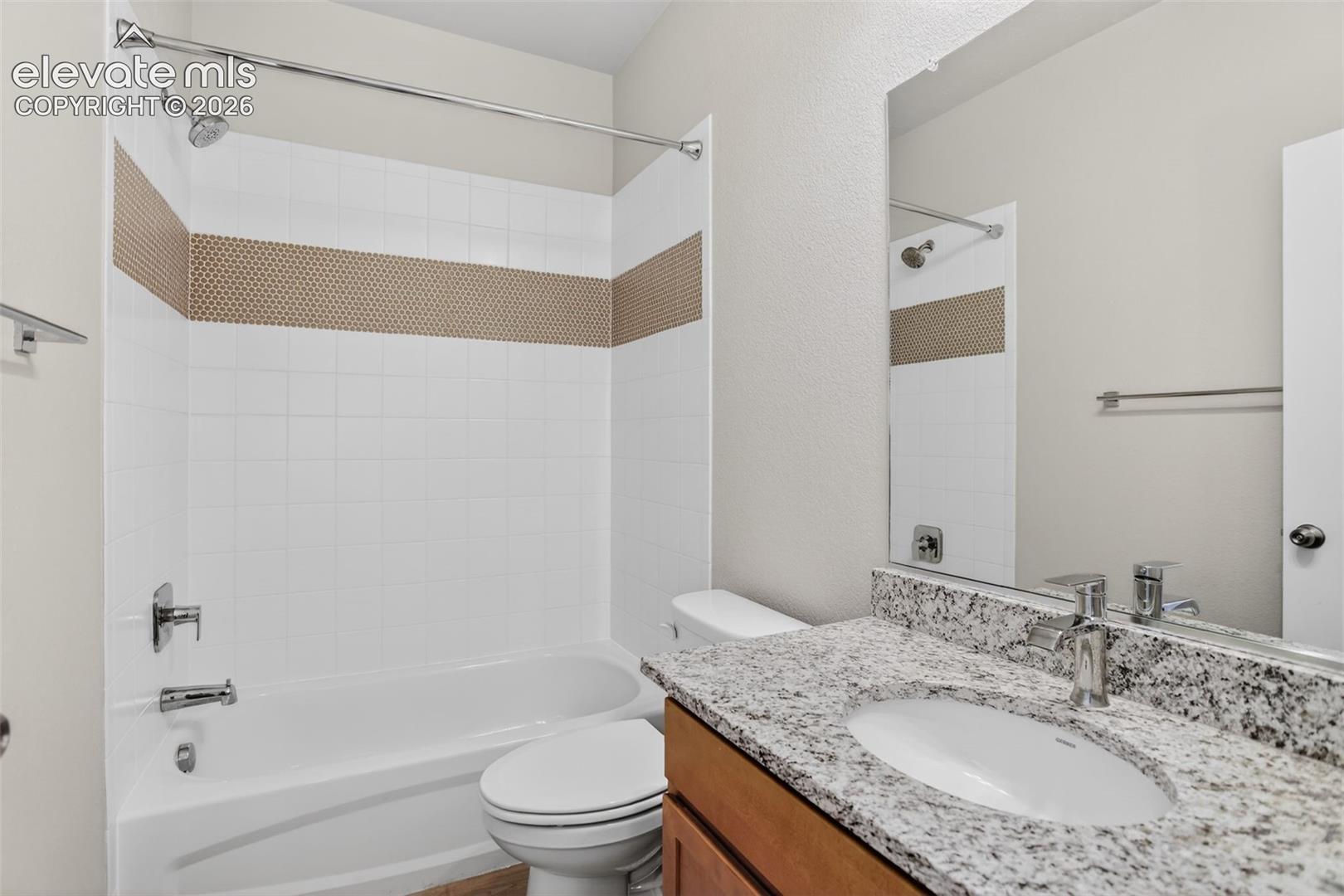 Bathroom featuring a white subway tile surround with a decorative mosaic accent band, a white porcelain tub, a toilet, a vanity with a granite countertop and an undermount sink, and chrome fixtures