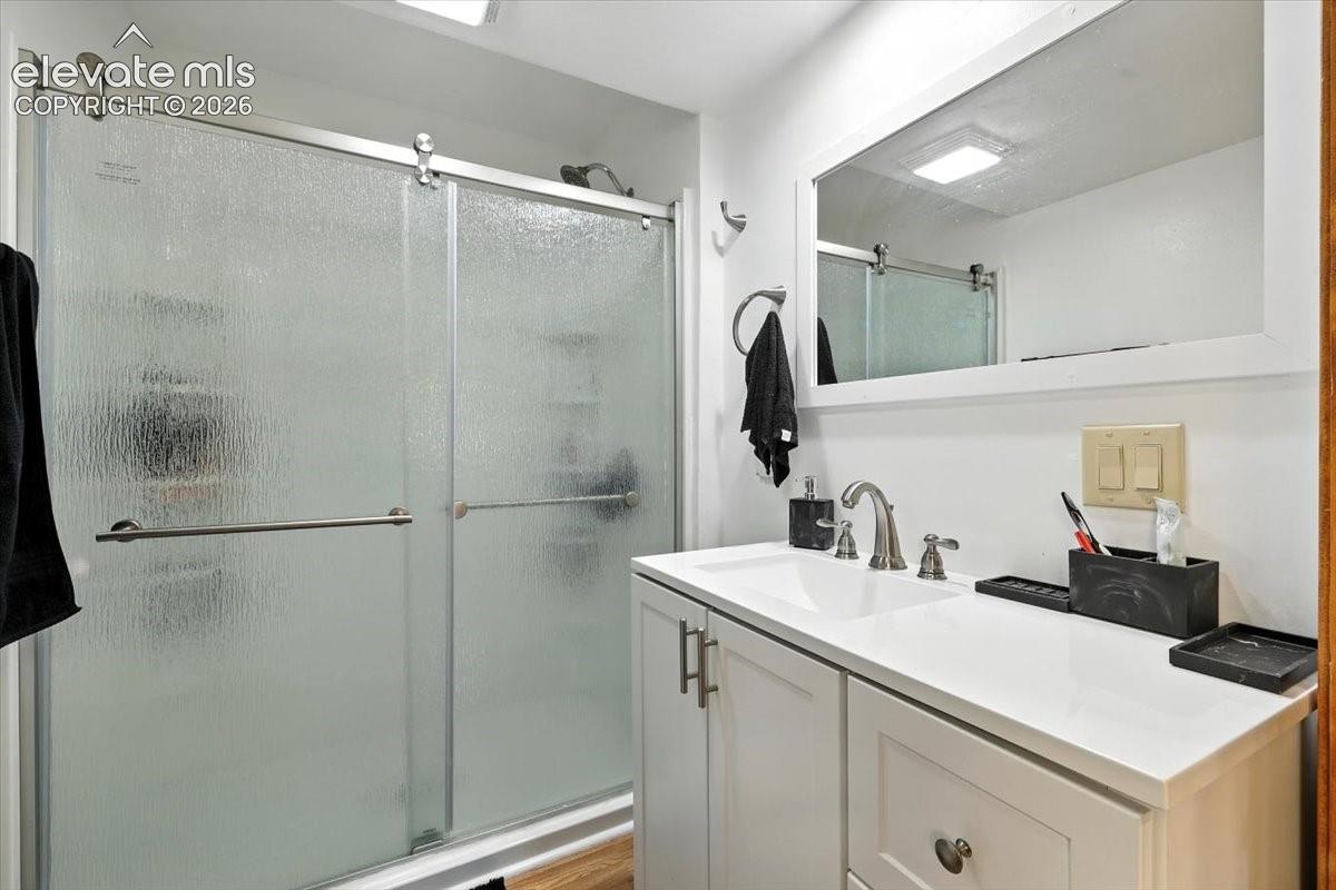 Bathroom featuring a vanity with a white countertop, integrated sink, and polished nickel faucet, accompanied by a framed mirror and a walk-in shower with a sliding glass door