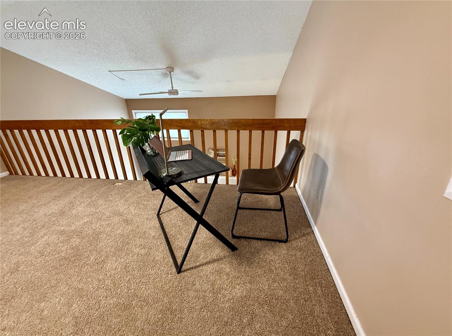 Loft space featuring vaulted ceilings, neutral carpeting, a wooden railing, and a ceiling-mounted fan in the living room area
