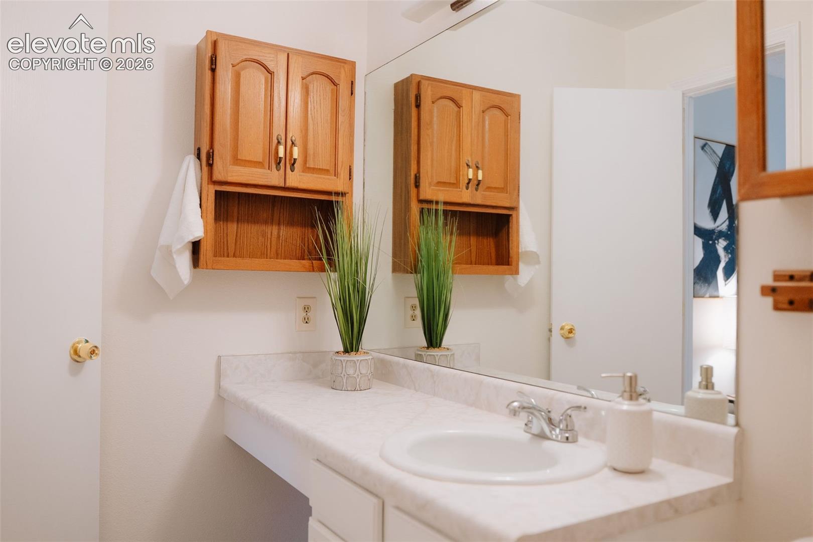 Bathroom vanity featuring a stone-finish countertop, integrated basin, dual-handle chrome faucet, wall-mounted wood cabinetry, and a large-format mirror