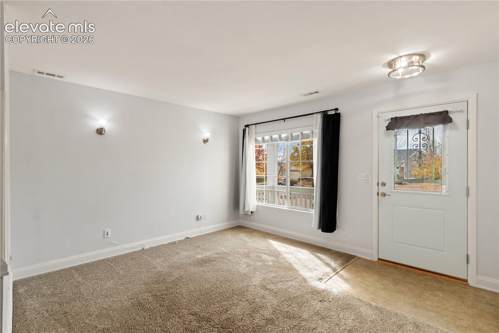 Neutral-toned wall finish with twin wall-mounted light fixtures, multi-pane window with grid detailing, and exterior door featuring an integrated decorative metal-grille window insert and ceiling-mounted flush-mount light