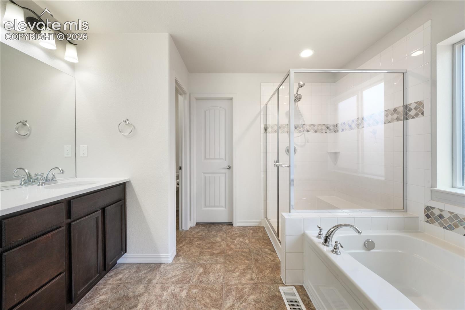 Main level primary 5 piece bathroom with dual sinks, granite counters, free standing shower, large bathtub, large walk in closet