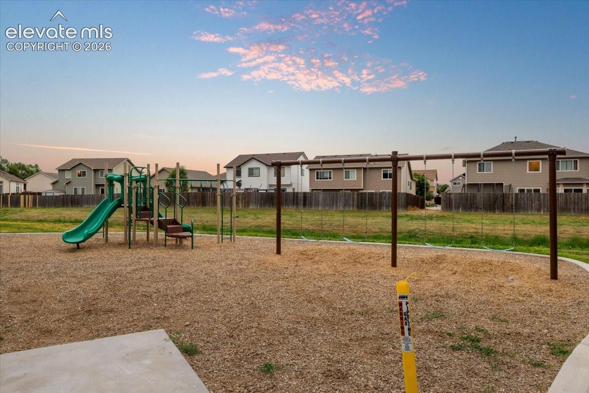 Community playground featuring a green slide, climbing structure, swing set, and wood chip surfacing