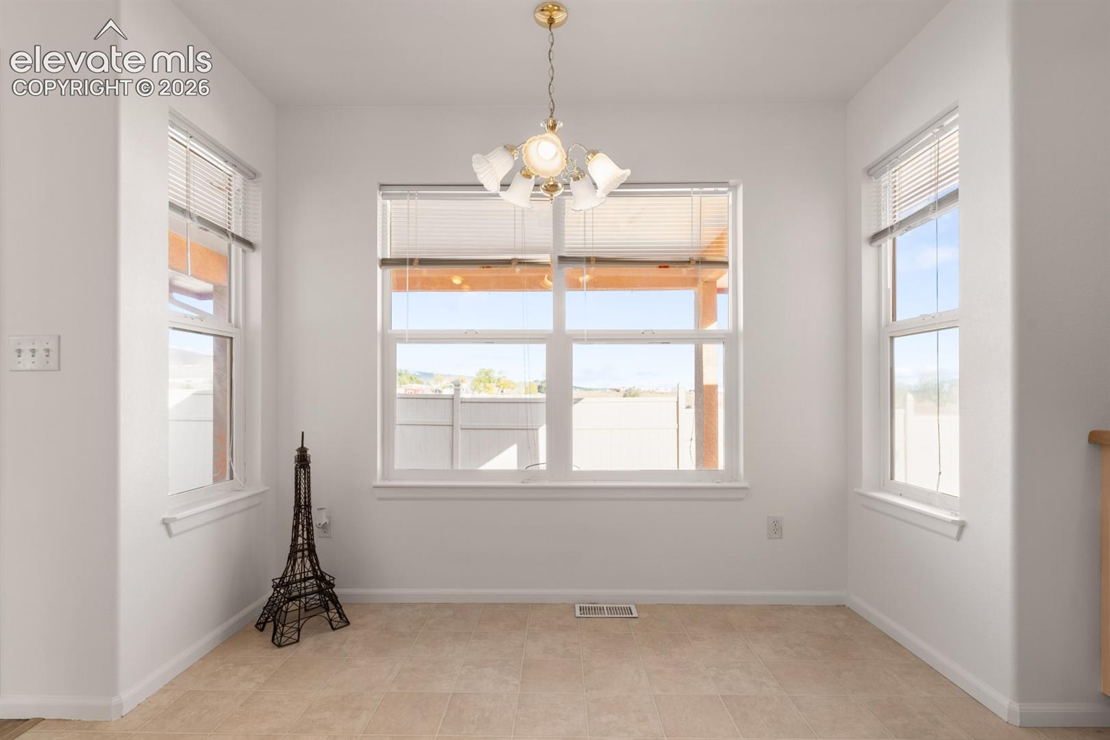 Bright, multi-windowed room featuring tile flooring, a centered multi-arm light fixture, and three large windows