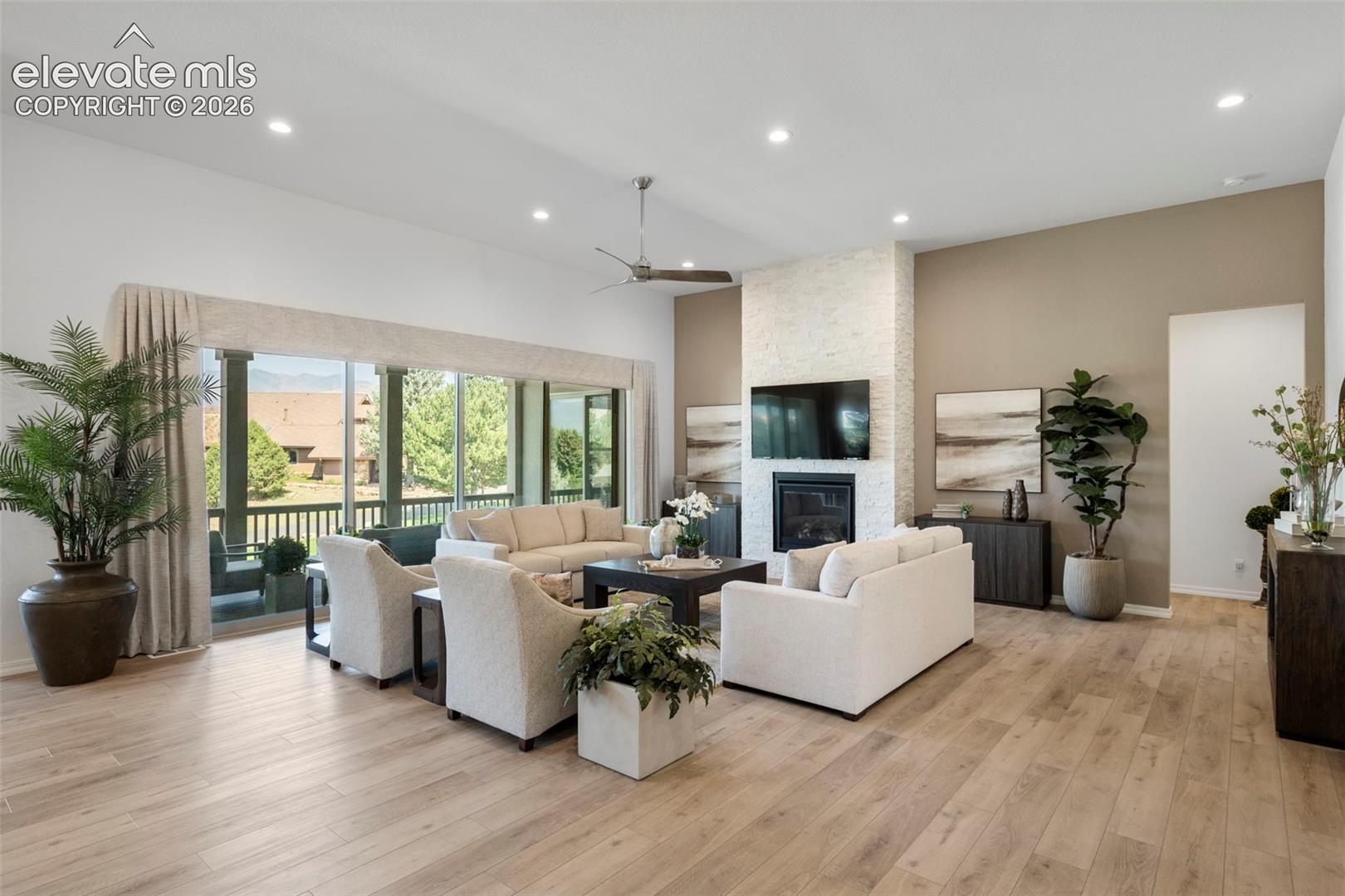 Grande ceilings with recessed lighting, beautiful flooring, floor to ceiling stone fireplace with mantel, and a sliding glass door to the covered outdoor living space