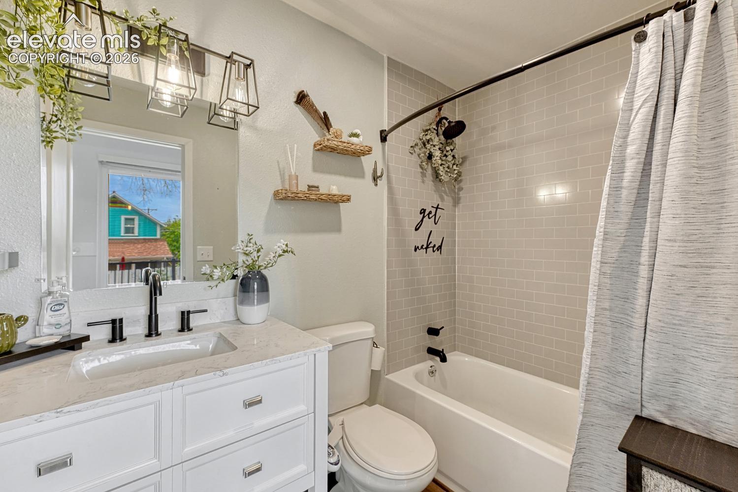 Bathroom featuring a white vanity with a quartz countertop and undermount sink, matte black faucet, and a mirror with industrial-style lighting overhead