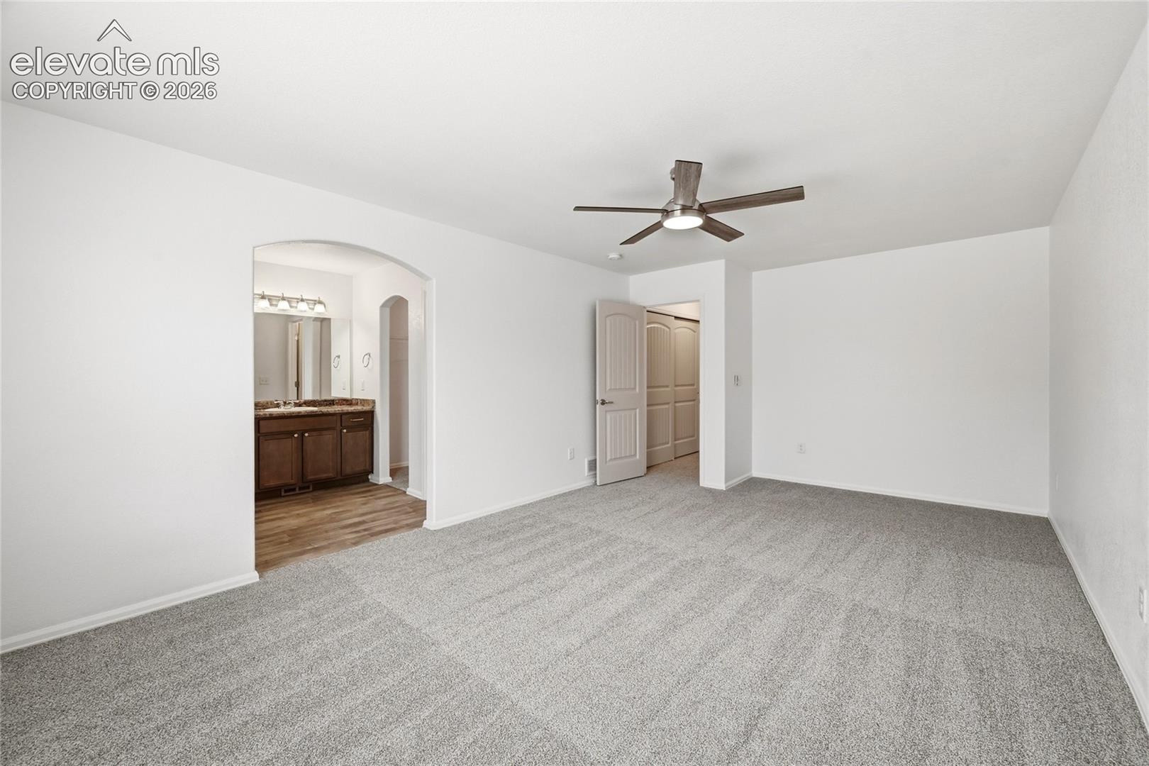 Neutral-toned carpeting, ceiling fan with integrated lighting, arched entryway, and multi-panel interior doors