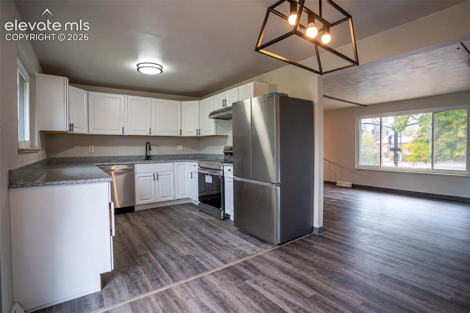 Kitchen featuring white cabinetry, stone-finish countertops, stainless steel appliances, wood-finish flooring, and a geometric metal pendant light