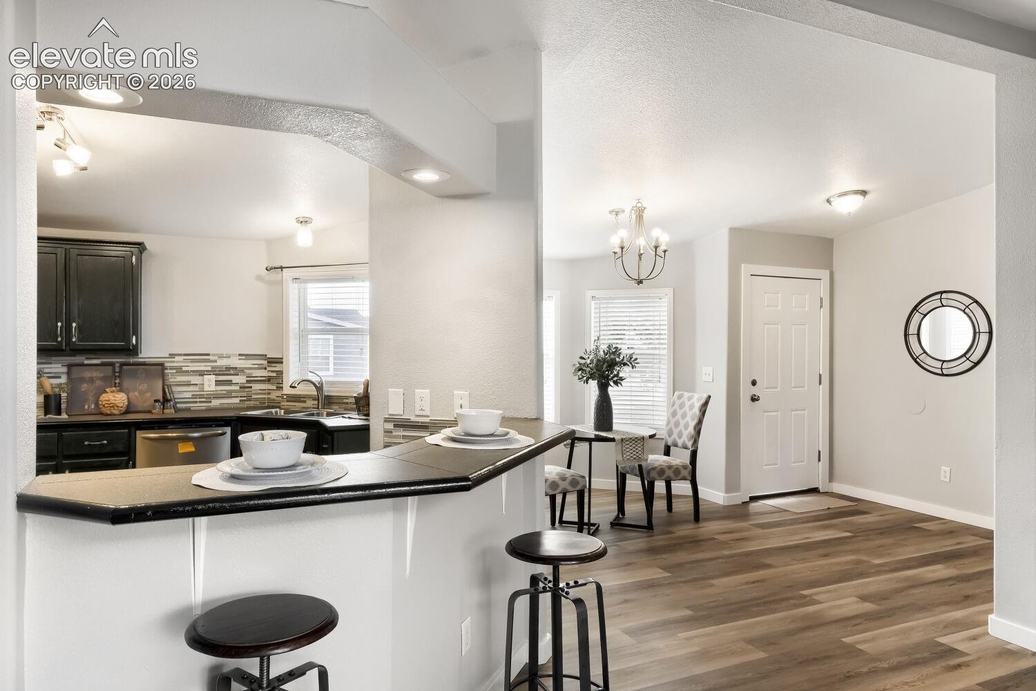 Kitchen featuring a breakfast bar with a solid surface countertop, dark cabinetry, tile backsplash, and wood-finish flooring
