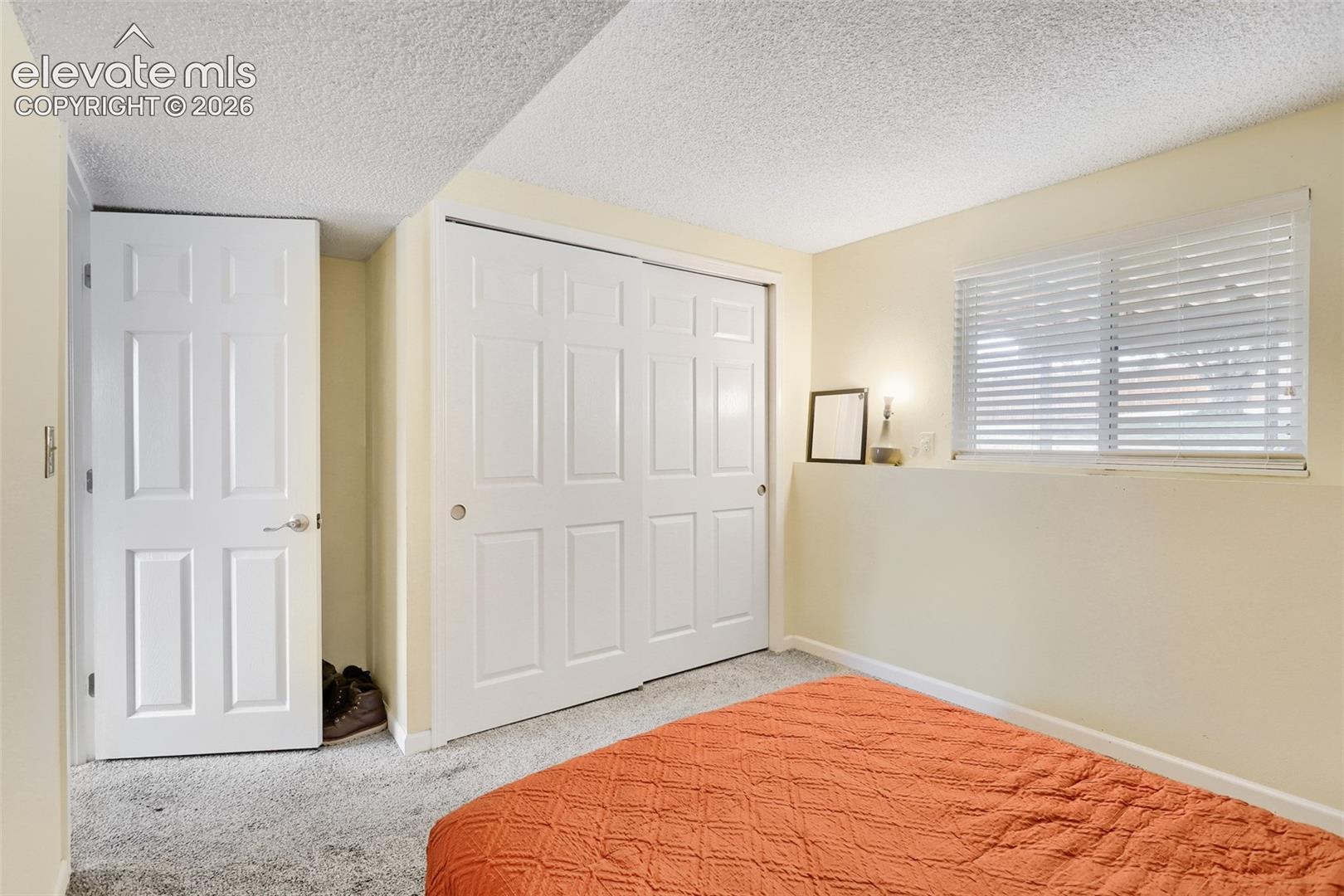 Room featuring light-colored walls, textured ceiling, a window with horizontal blinds, and paneled doors