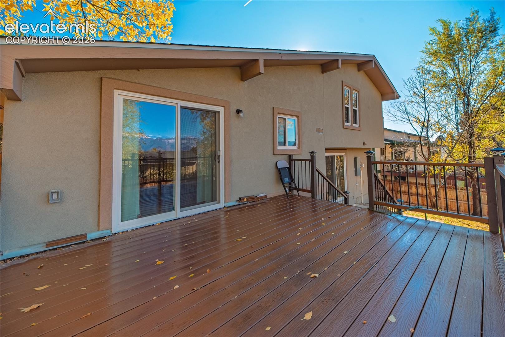 Stucco exterior with a sprawling wood-finish deck, sliding glass door, and metal railing