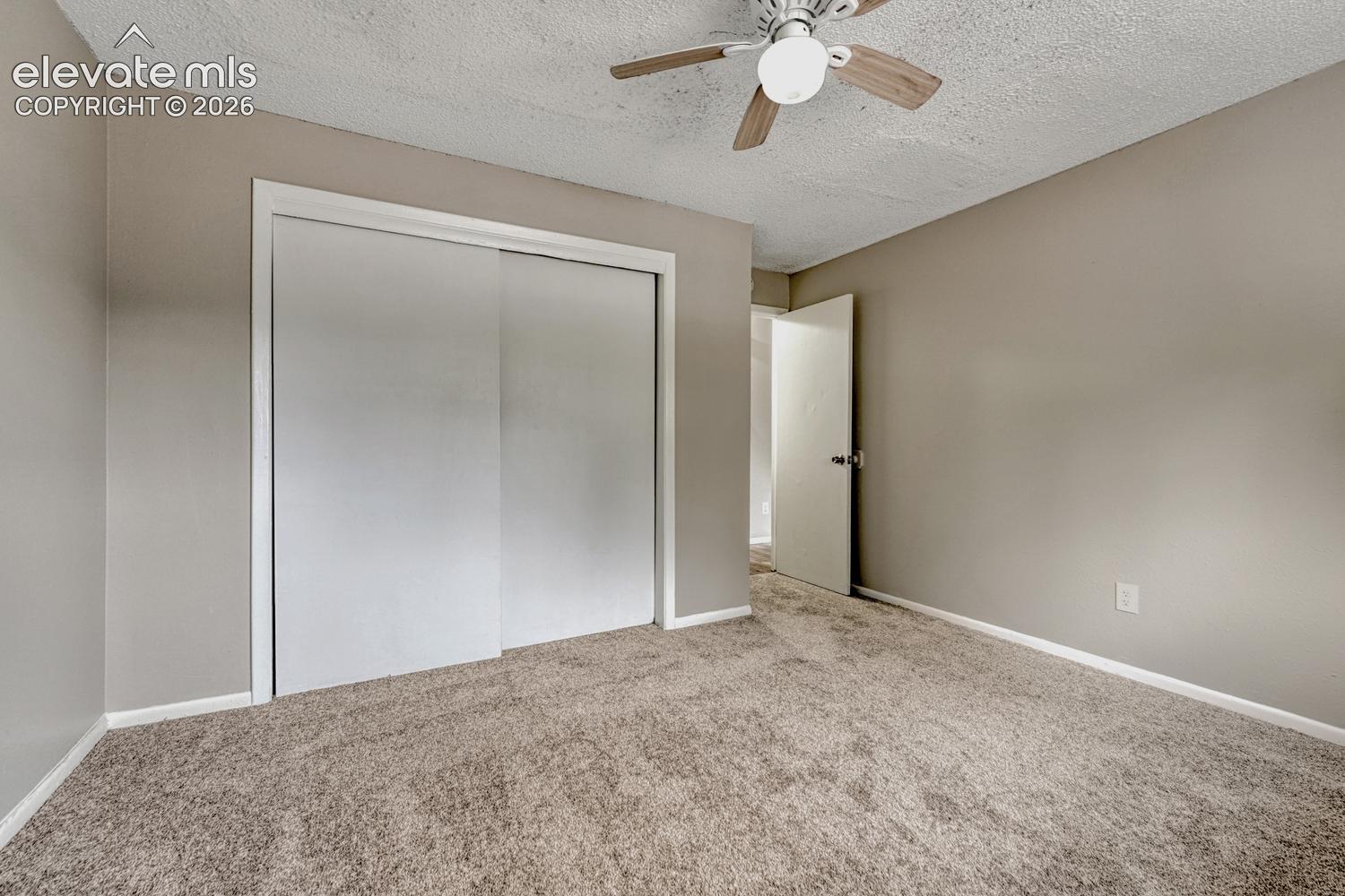Textured ceiling with a ceiling fan, neutral wall paint, white trim, carpeted flooring, and a sliding closet door