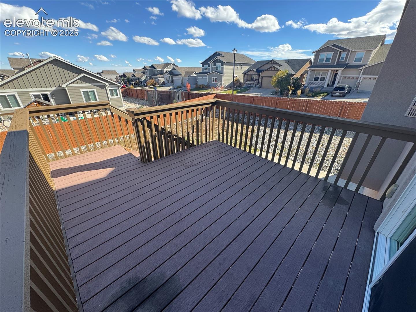 Elevated deck featuring composite planking and vertical wood-slat railing, overlooking a fenced backyard with decorative gravel ground cover