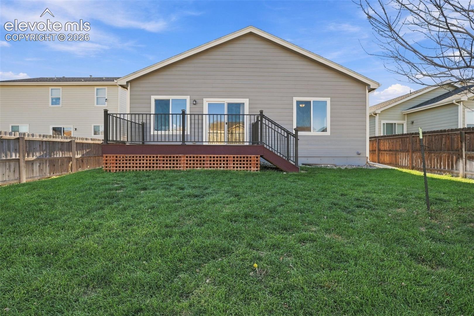 Rear exterior featuring horizontal lap siding, an elevated wood deck with metal railings, lattice skirting, and a fenced backyard