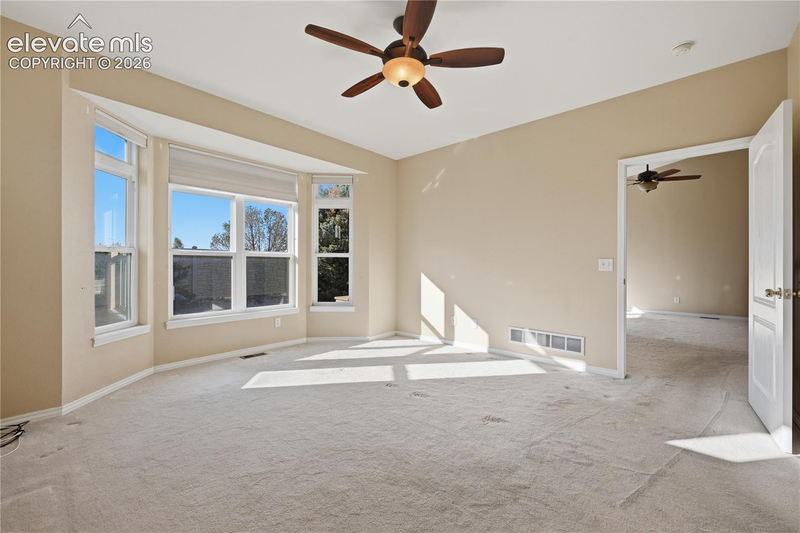 Bay window with multiple panes, neutral wall palette, overhead ceiling fan with light kit, and carpeted flooring