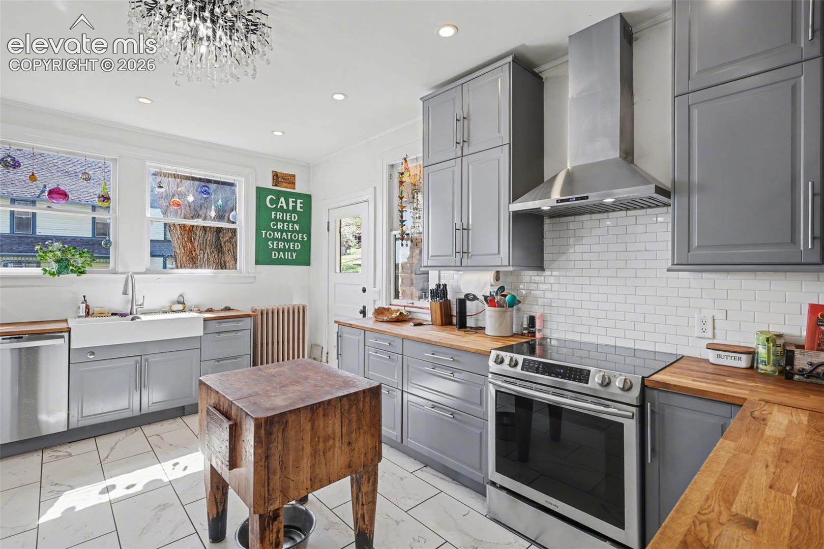 Main house kitchen featuring gray cabinets, light tile, wood counters, and recessed lighting