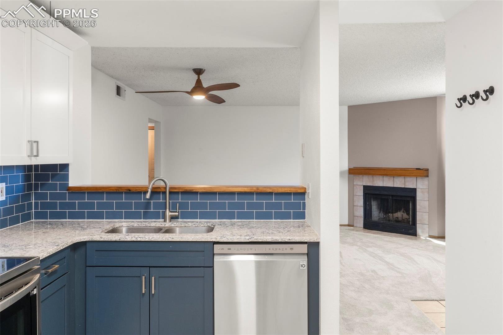 Kitchen featuring a fireplace, stainless steel appliances, light colored carpet, light stone counters, and decorative backsplash