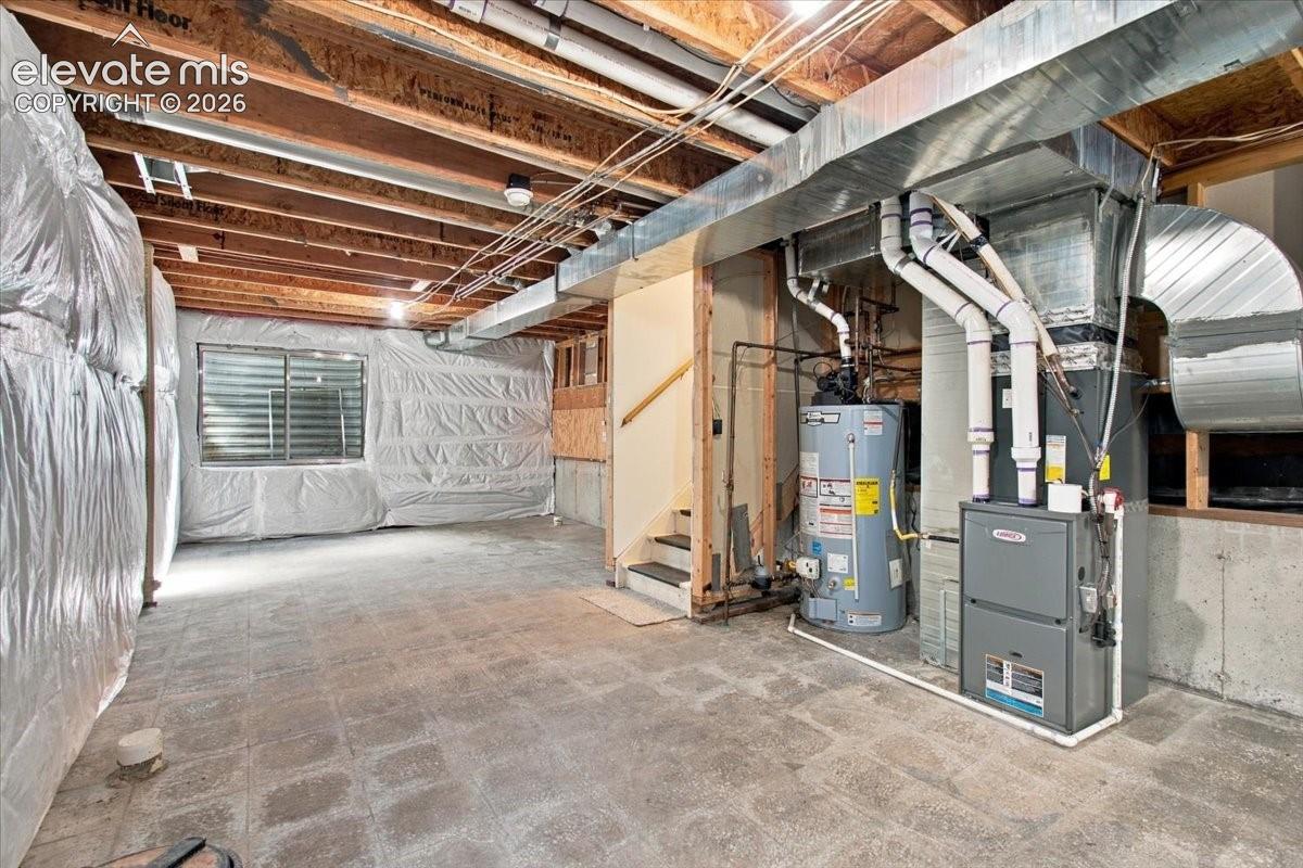 Unfinished lower level featuring exposed joist ceilings, concrete foundation walls with vapor barrier insulation, a central heating furnace, and a dedicated water heater