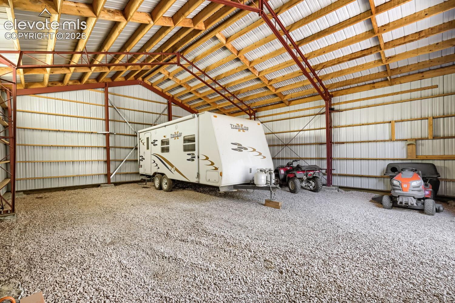 Spacious outbuilding featuring a durable gravel floor, exposed wood ceiling beams, and corrugated metal walls