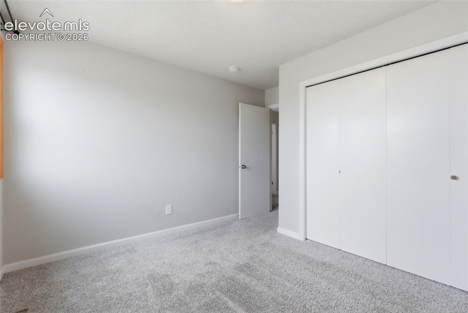 Neutral-toned bedroom featuring wall-to-wall carpeting, light gray wall paint, white baseboards, and a white bi-fold closet door
