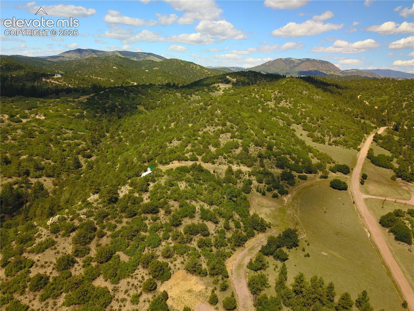 Expansive land parcel featuring rolling hills, mature tree coverage, a natural clearing, and distant mountain backdrops